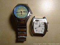 Photo showing both Perry Ellis watches side by side, one with blue-green dial and metal band, second missing band.