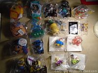 Overview of 17 McDonald's toys all still sealed in original plastic packaging spread on a table, showing variety including plush and plastic toys.
