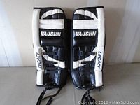 Front view of both Vaughn Legacy goalie pads side by side showing black and white color scheme and branding.