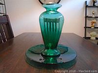 Green glass vase and matching plate set shown from a front angle on a wooden table.