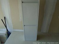 Front view of the tall white metal cabinet showing two distinct drop-down doors in good condition