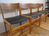 Row of four teak chairs against a wall
