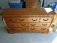 Front view showing entire wooden dresser with seven drawers, decorative carved trim, and metal handles.