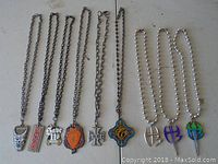 Full view of 9 metal necklaces hanging, each with unique pendant including skull, text, flame, crosses, and emblems