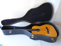 Opened black hard shell guitar case with acoustic guitar inside showing natural wood finish and nylon strings.
