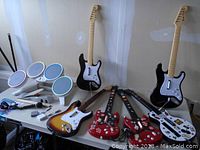 Guitar-style gaming controllers in black, sunburst, and red colors with a microphone and other accessories