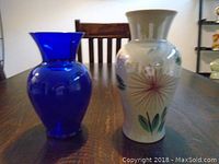 Two vases side by side on wooden table: one cobalt blue glass vase and one ceramic vase with floral painting