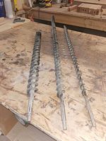 Three long steel auger bits on workbench