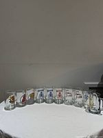 Front view of ten clear glass beer mugs lined up showing various decals