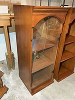 Front view of wood display cabinet showing arched glass door and shelves