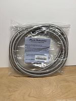 Front view of coiled stainless braided hose in sealed plastic with label