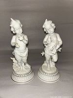 Front view of both bisque putti figurines on bases