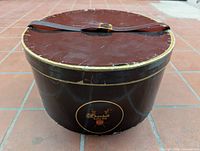 Full view of cylindrical Churchill Ltd hat box with lid and leather strap