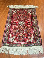 Full view of red Persian Sarouk rug with fringes displayed on wood floor