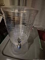 Side view of clear ribbed plastic beverage dispenser showing spigot