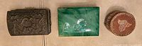 Three boxes side by side: brass carved box, green marble box, birch bark quill container
