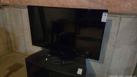 Front view of LG TV on stand with remote and power cord visible