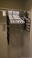 Closet rod showing white plastic hangers, metal clip hangers, black pants hanger and fabric organizer
