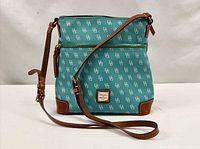 Front view of teal monogram crossbody showing strap, front zip pocket and logo plaque