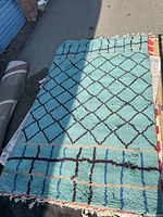 Full view of turquoise/teal wool rug showing geometric diamond pattern and fringed edge