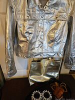 Full view metallic jacket hanging, gold-tone tote below, cuffs and belts partially visible