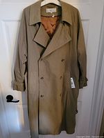 Front view of olive-beige Yves Saint Laurent double-breasted trench coat on hanger
