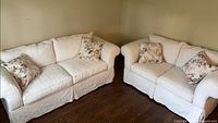 Both white slipcovered loveseats with floral pillows