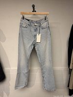 Front view of light blue denim jeans hung on hanger