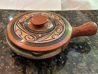 Side view of lidded redware casserole showing handle, glaze and painted design