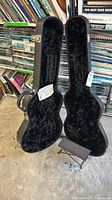 Open black hardshell acoustic guitar case with black plush interior and folding footrest visible