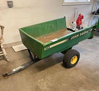 Full view of green John Deere dump cart with tow bar