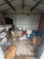 Overview of shed interior showing sinks on shelf, boxes, lamp, bucket, crates