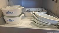 Drawer containing two CorningWare casseroles with lids, one rectangular baker in cradle, and four oval gratin dishes