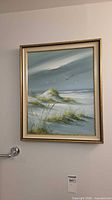 Painting of dunes, grasses and seagulls in gold frame on wall