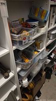 Shelves with plastic bins containing mixed hardware, tools, gloves and storage tubs