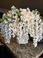 Front view of entire floral arrangement showing cascading white wisteria blossoms and vase on granite counter