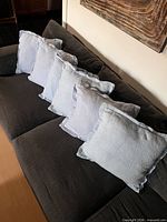 Five of the six light blue raw-edge throw pillows arranged on a dark sofa