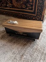 Top and side view of wooden music jewelry box showing lid ornament, wood-grain finish, black lacquer body and gold scrollwork