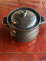 front view of black glazed ceramic pot with lid on wooden surface