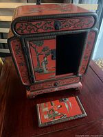Front view of red lacquer cabinet showing door open and drawer panel