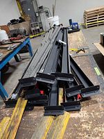 Pile of black steel shelf support rails stacked on workbench