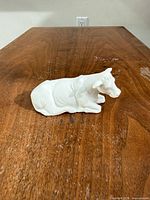Front left view of white bisque porcelain cow figurine on wooden surface