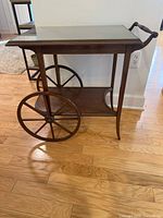 Front view of wood tea cart showing wheels, shelves, handle, and glass top