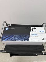 Sealed HP 134X toner cartridge box on fabric drawer of cart