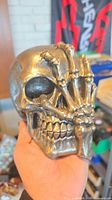 Front view of metallic silver skull figurine with skeletal hand detail