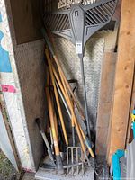 Bundle of long wooden-handled tools including plastic leaf rake and assorted shovels