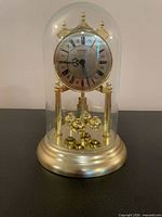 Full view of Danbury brass torsion clock under glass dome showing base, dial, and pendulum