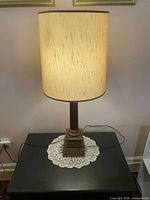 Full view of lamp with shade on tabletop, doily underneath