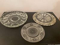 Three clear glass platters laid out showing patterns
