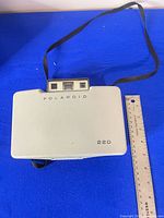 Closed Polaroid 220 camera with strap beside ruler